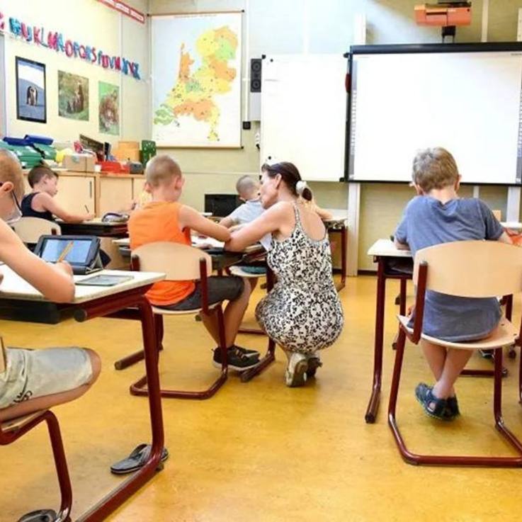 Unterricht im Klassenraum mit Blick von den hinteren Reihen nach vorn zur Tafel - schreibende Schulkinder