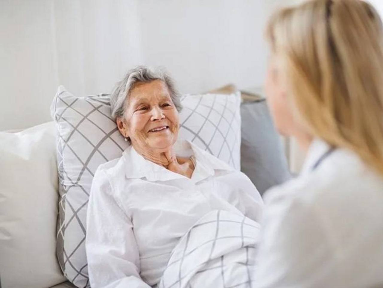 Ältere Dame, angelehnt im Bett sitzend wird von einer jüngeren Frau besucht
