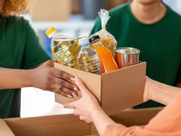 Übergabe eines Kartons voller Lebensmittel - Öl, Saft, Wasser, Nudeln, Konserve ...