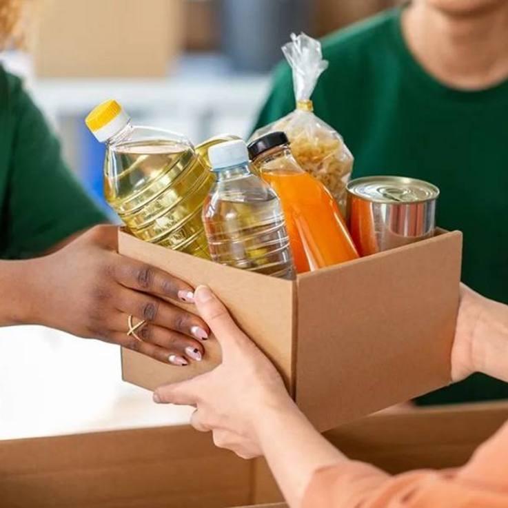 Übergabe eines Kartons voller Lebensmittel - Öl, Saft, Wasser, Nudeln, Konserve ...