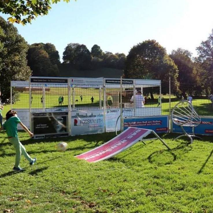 Kinder spielen im Soccer Cage und an der Fußballrampe mit Fangkorb des auf sonniger Wiese im Freien aufgebauten Funparks