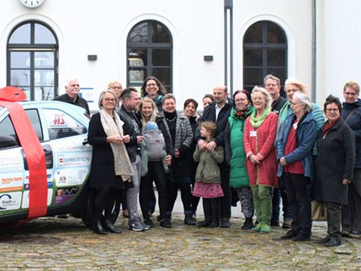 Folierter gesponsorter Toyota Aygo X mit roter Schleife darum links von den Sponsoren und Mitwirkenden des Hospizvereins Lüchow-Dannenberg