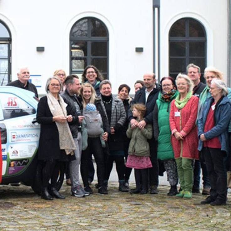 Folierter gesponsorter Toyota Aygo X mit roter Schleife darum links von den Sponsoren und Mitwirkenden des Hospizvereins Lüchow-Dannenberg