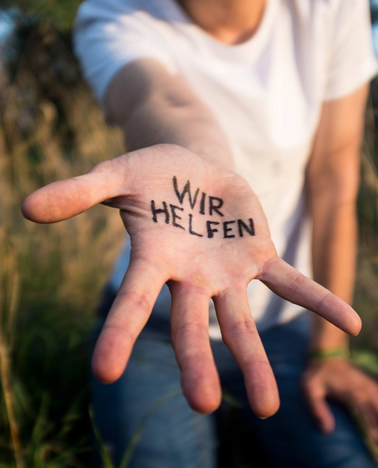 "WIR HELFEN" in den dem Betrachter entgegengestreckten rechten Handteller geschrieben