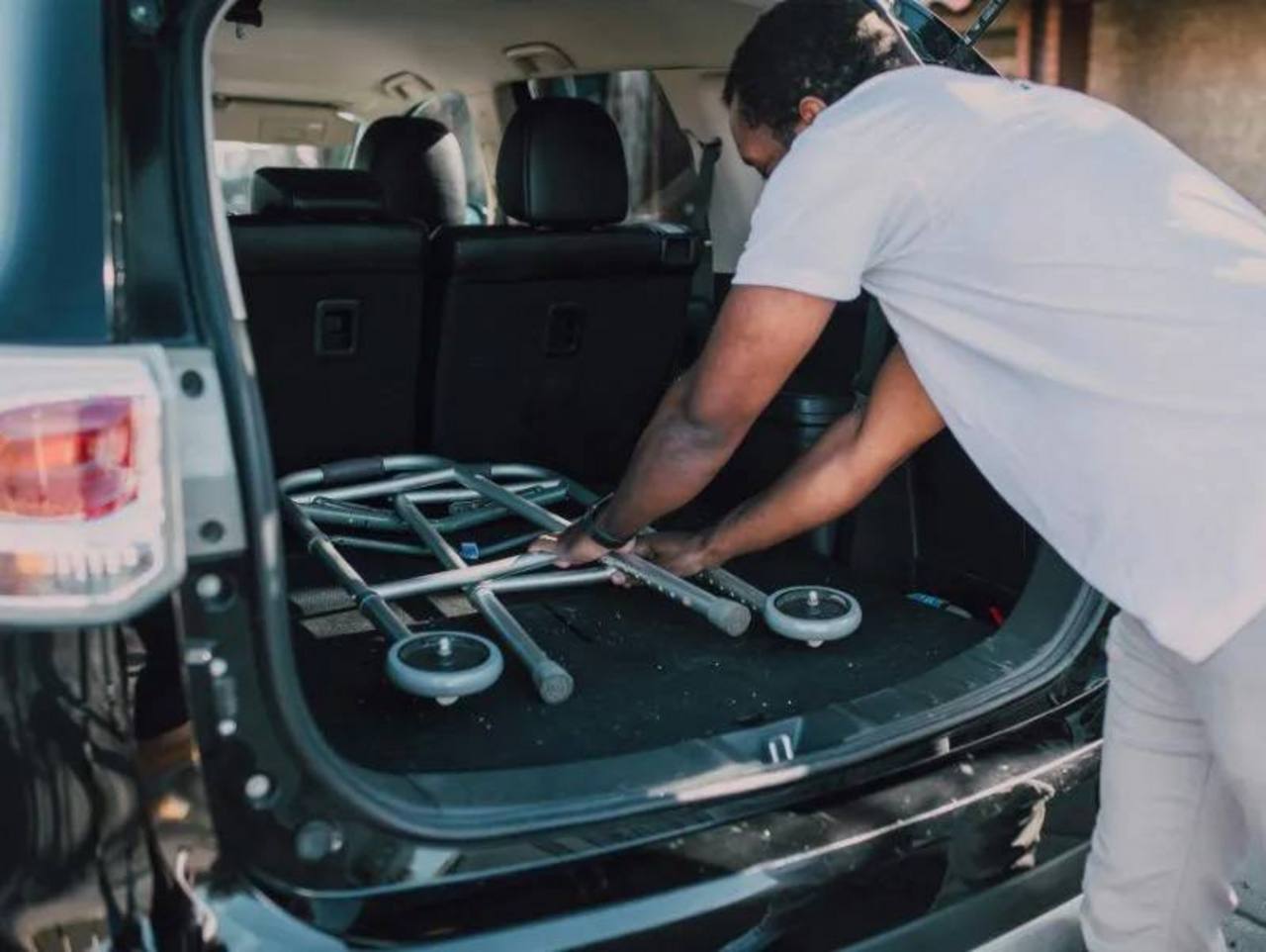 Ein Mann lädt eine Gehhilfe in den offenen Laderaum eines schwarz lackierten Transporters