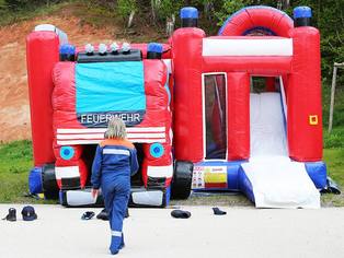 Hüpfburg in Form eines Feuerwehrautos zum Klettern, Springen und Rutschen - Blick auf die Front mit darauf zulaufendem Kind - Feuerwehrhüpfburg